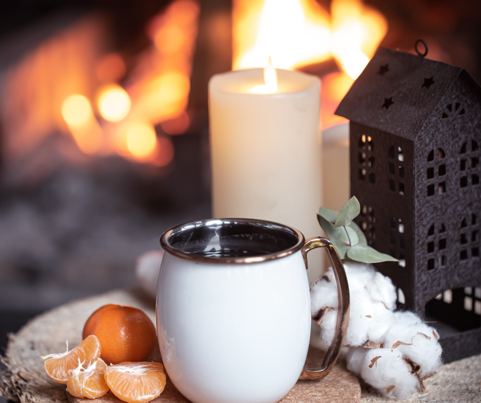 A calm evening setting, with a live fire, tea cup, orange pieces and a lit candle