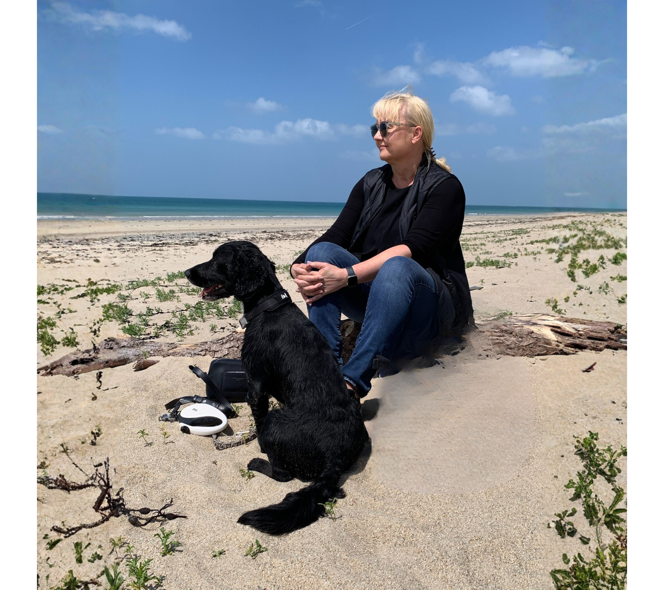 Lykke & Lumen founder Marie-Louise sitting on a beach with her dog Romeo, looking out across the sea during a moment of quiet reflection.