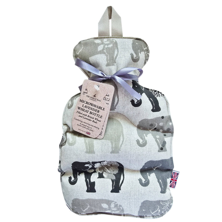 A fabric wheat bottle with an elephant print pattern in black, grey, and beige, tied with a lavender ribbon and featuring a paper tag that reads 'MICROWAVEABLE WASHABLE WHEAT BOTTLE'.