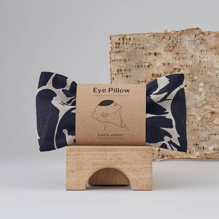 Eye pillow with floral pattern on a wooden stand against a neutral background