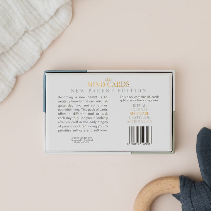 Pack of 'New Parent Edition' mind cards on a light surface with a baby rattle and blanket.