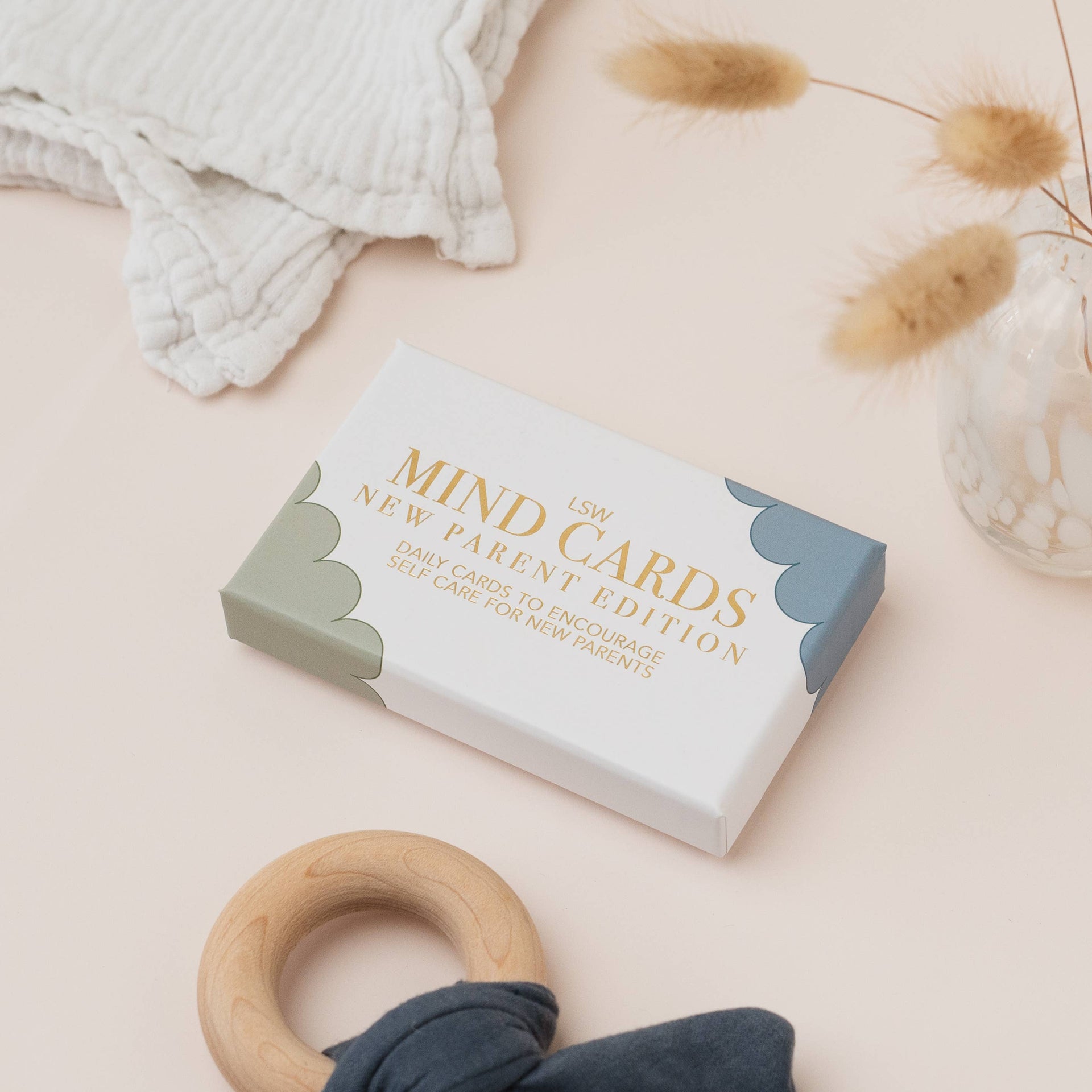 Box of 'MIND CARDS New Parent Edition' on a light surface with a wooden ring and textured fabric.
