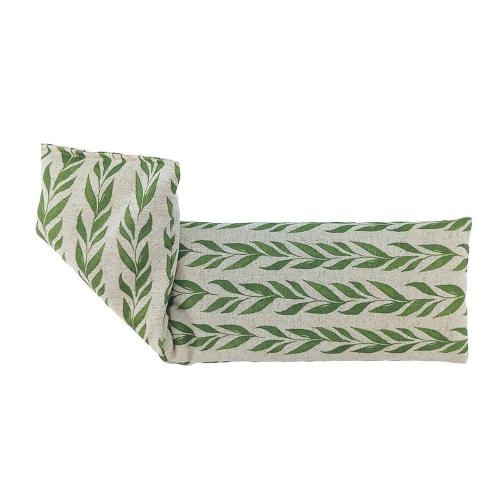 A rectangular wheat bag with a green leaf pattern on a light beige linen-textured fabric, shown folded on a plain white background.