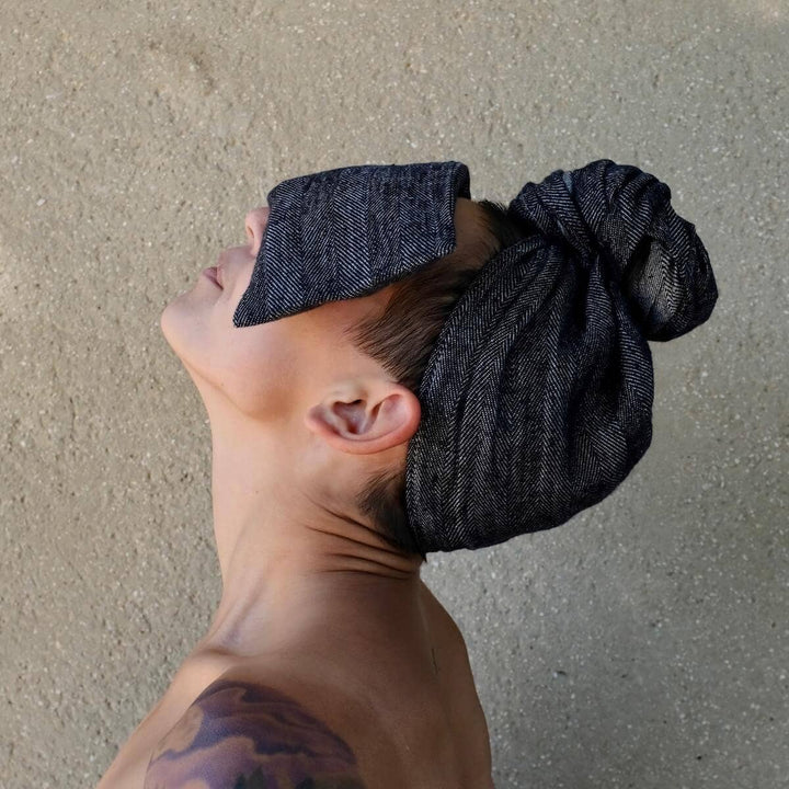 Person wearing a dark gray textured headscarf and eye pillow against a plain background