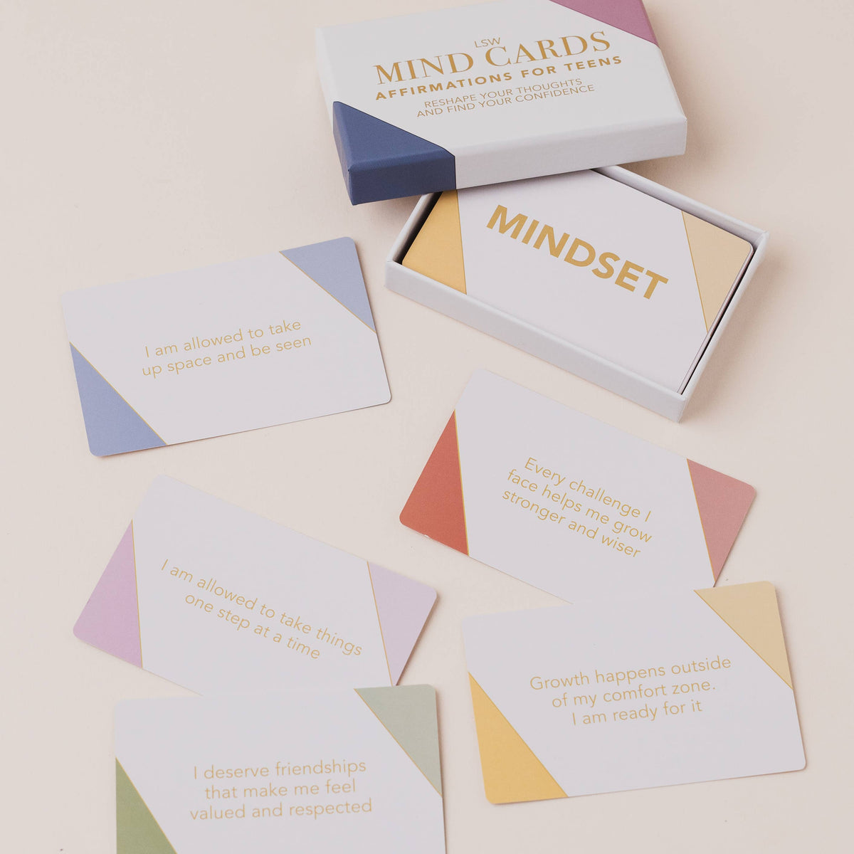 A set of affirmation cards for teens with their branded box, arranged on a light beige background. The cards are white with geometric color blocks in pastel blue, purple, orange, yellow, and green, and feature positive quotes printed in gold.