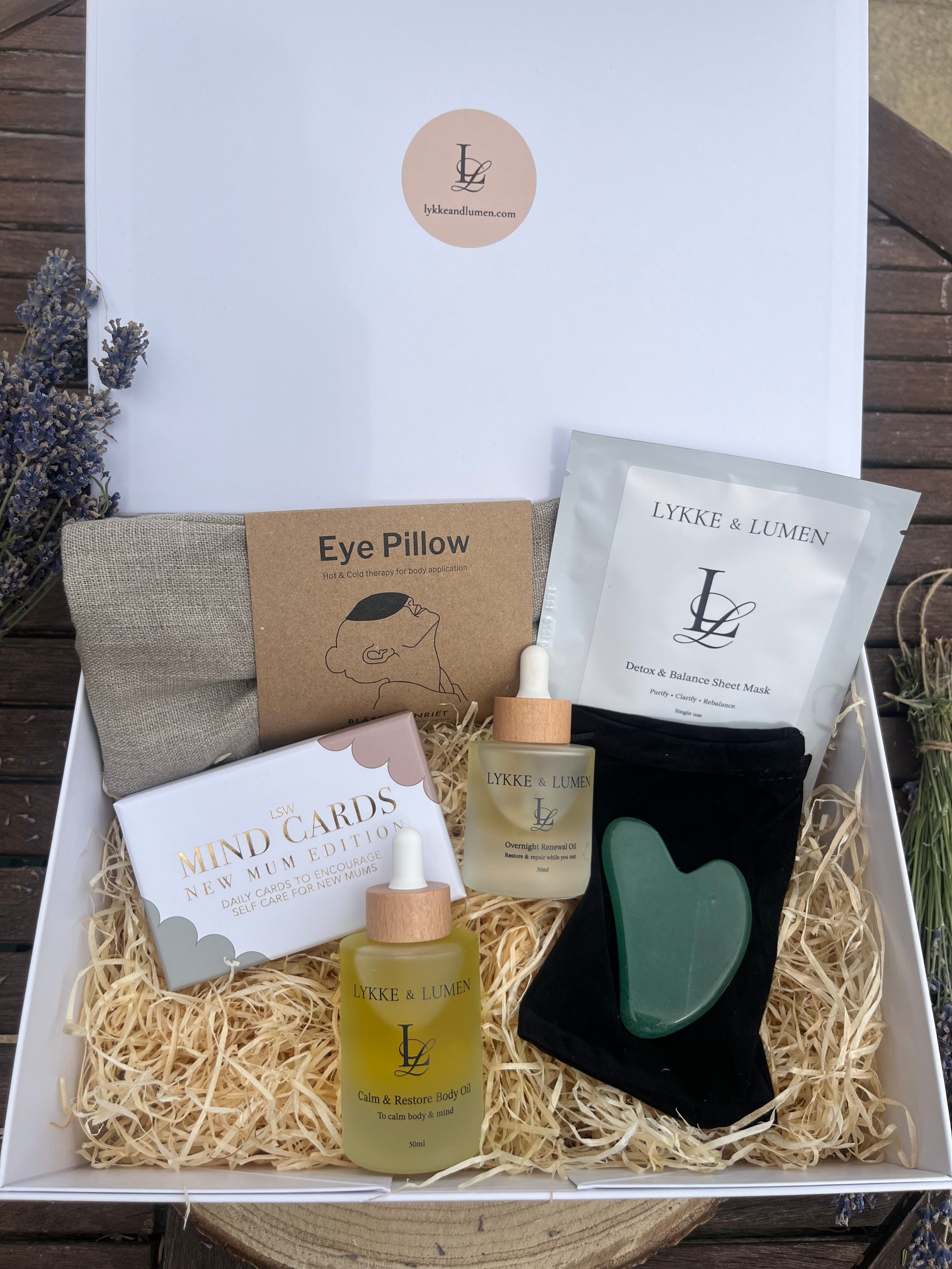 A curated gift box set from Lykke & Lumen, featuring an eye pillow, facial gua sha tool, Overnight Renewal Oil, Calm & Restore Body Oil, Mind cards and a Detox & Balance Sheet Mask. Arranged in shredded wood inside a white magnetic gift box.