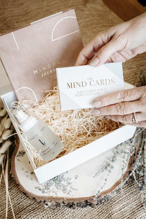Hand holding a card with 'The Mind Cards' text, Lykke & Lumen wellness gift set featuring Relax & Reset Mist, mindfulness cards and a mindful journal presented in a luxury self-care gift box with calming natural styling.