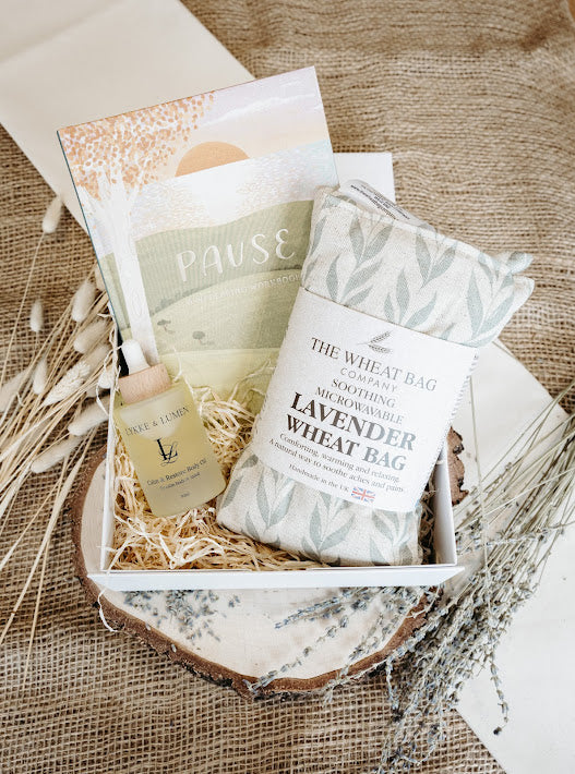 Lykke & Lumen wellness gift box featuring Calm & Restore Body Oil, a lavender wheat bag and wellbeing workbook styled in a luxury self-care setting with natural textures and dried botanicals.
