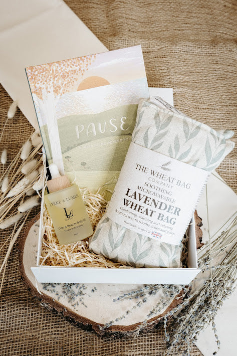 Wellbeing and Relaxation Gift set with lavender wheat bag, Lykke & Lumen Calm & Restore Body Oil and a pause journal on a wooden surface