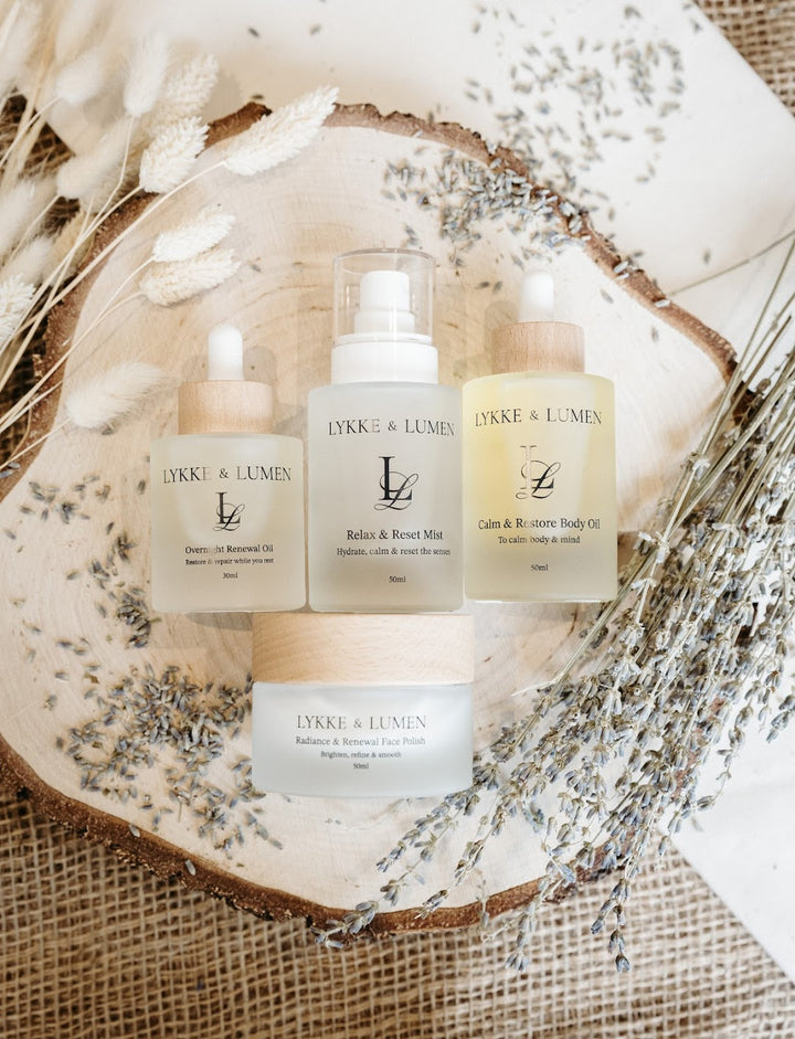 Lykke & Lumen skincare ritual collection featuring Overnight Renewal Oil, Relax & Reset Mist, Radiance & Renewal Face Polish and Calm & Restore Body Oil styled with dried lavender in a calming wellness setting.