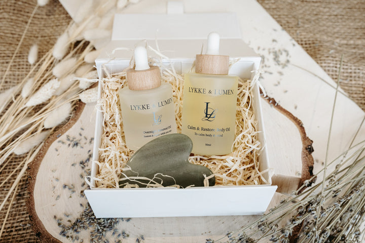 Luxury Lykke & Lumen wellbeing skincare gift set featuring Overnight Renewal Oil, Calm & Restore Body Oil and a gua sha tool presented in a white magnetic gift box with dried lavender styling.