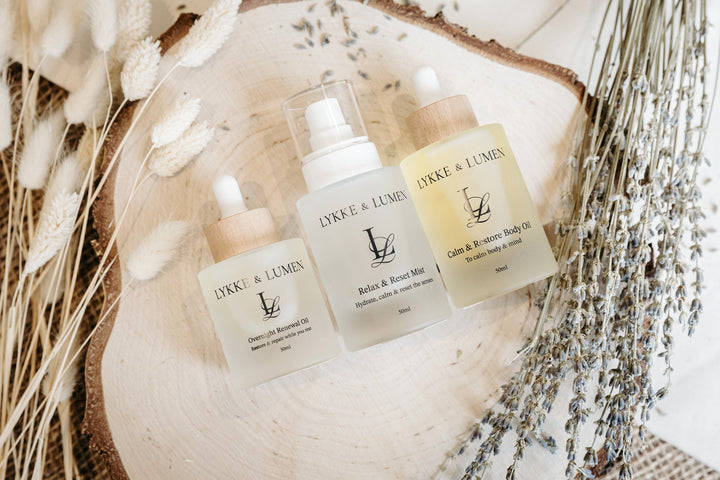 Lykke & Lumen skincare ritual collection featuring Overnight Renewal Oil, Relax & Reset Mist and Calm & Restore Body Oil styled with dried lavender in a calming wellness setting.