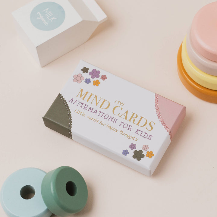 Box of 'Mind Cards for Kids' on a light pink background with colorful objects around.