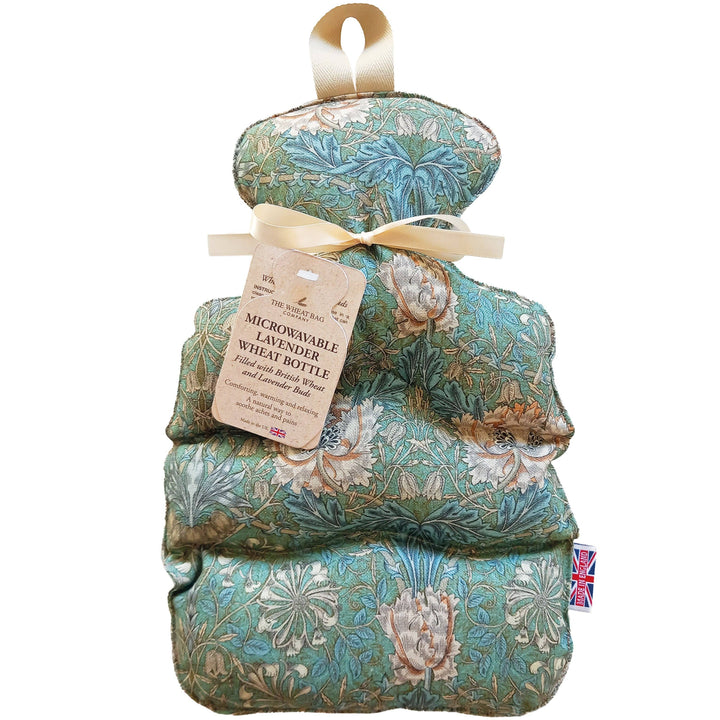 A quilted hot water bottle bundle with a floral William Morris-style print in teal, beige, and brown, tied with a cream ribbon and a paper tag that reads 'MICROWAVEABLE LAVENDER WHEAT BOTTLE'.