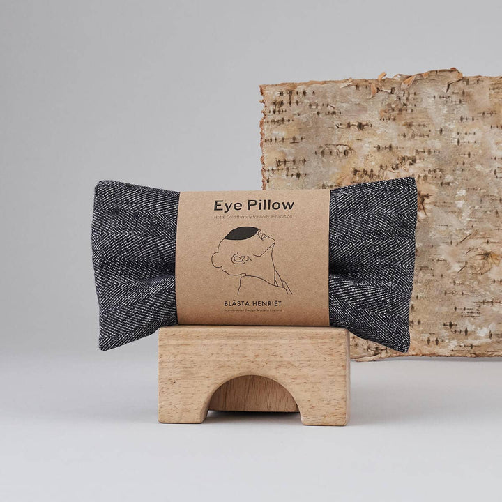 Eye pillow with a branded packaging label on a wooden stand against a neutral background