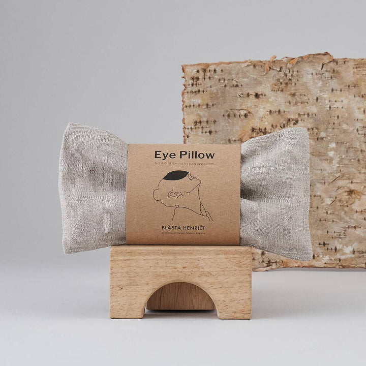 Plain beige Eye pillow with packaging on a wooden stand against a neutral background