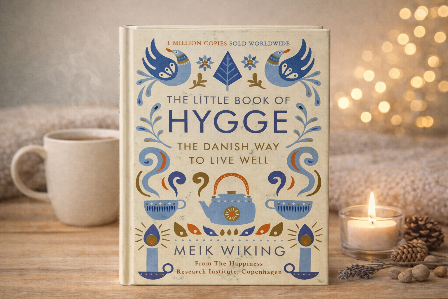 Book titled 'The Little Book of Hygge' on a wooden surface with a cup, candle, and decorative elements.